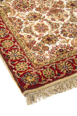 Primer plano de alfombra de estilo clásico con diseño floral elegante, guarda roja decorativa y flecos beige en un extremo.