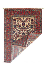 Alfombra persa rectangular con esquina doblada, guarda roja y diseño floral ornamental.