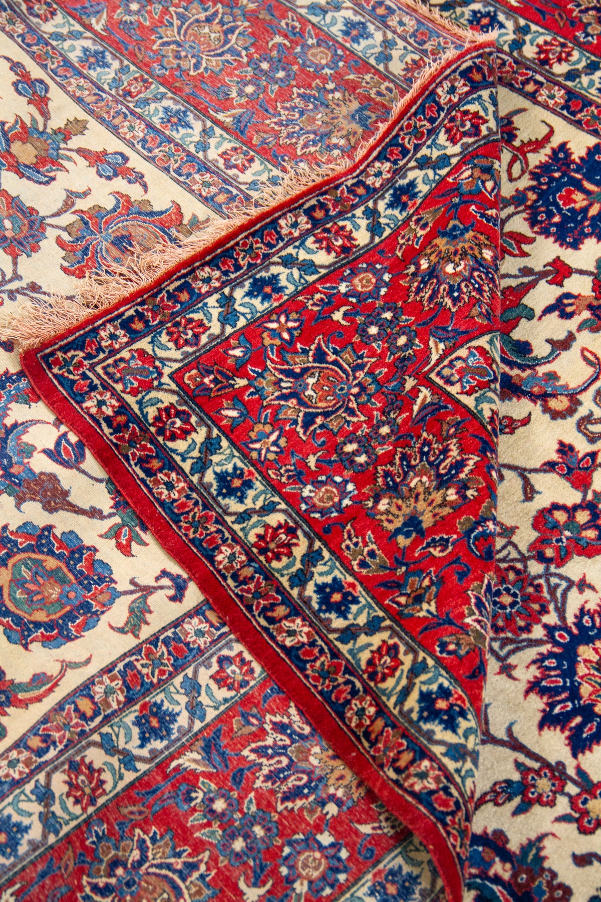 Detalle de textura y pliegue de alfombra persa con diseño floral en rojo, beige y azul