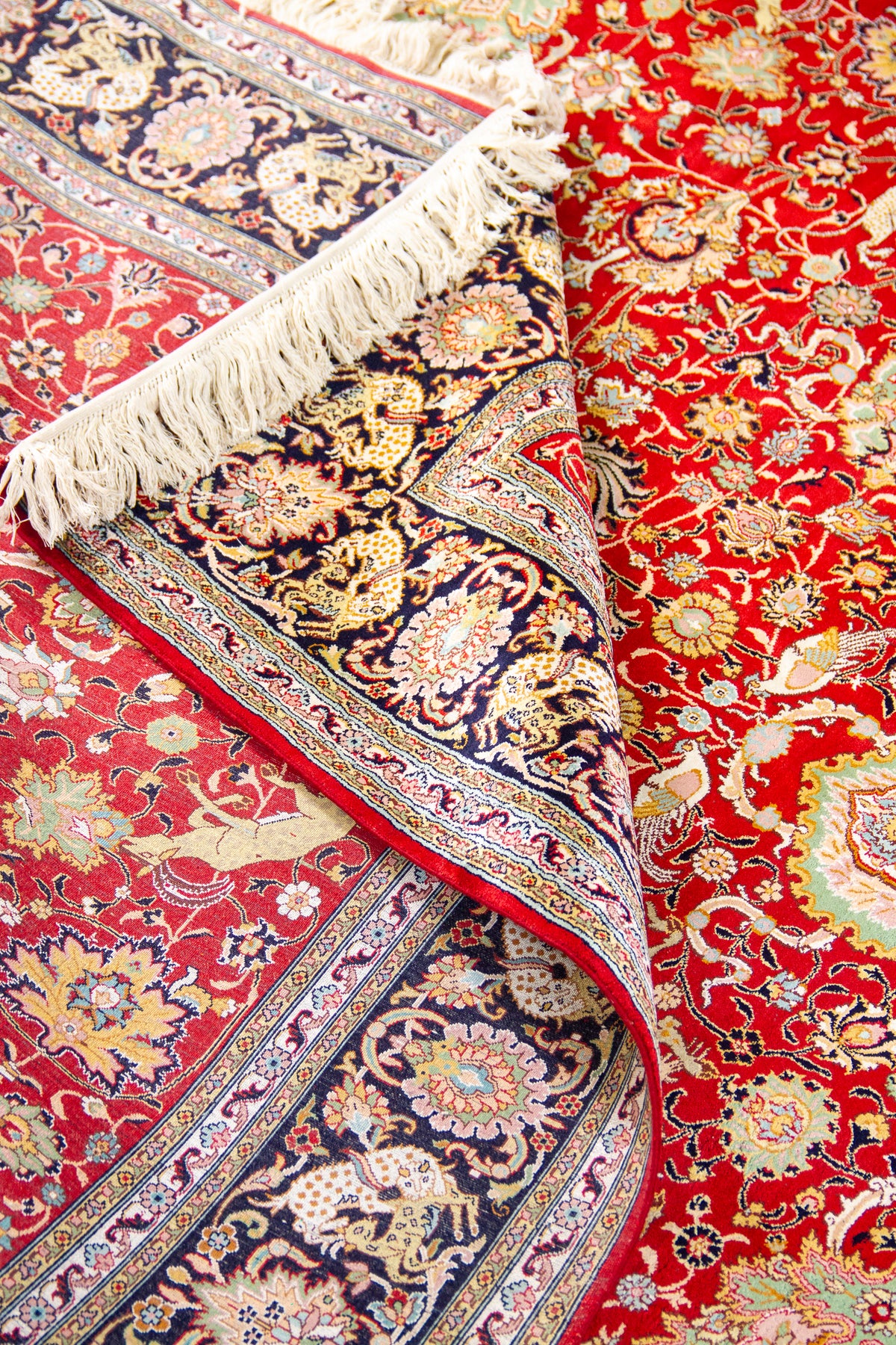 Detalle de textura y pliegue de alfombra persa roja con guarda oscura y diseño floral