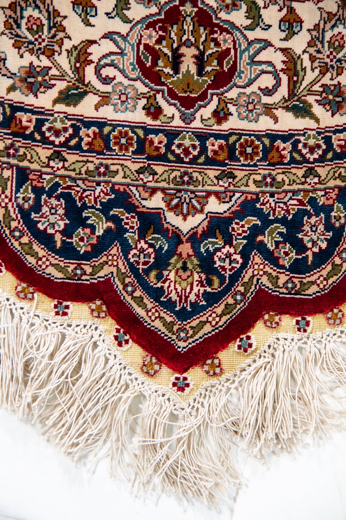 Detalle de guarda y flecos de alfombra persa redonda con diseño floral y tonos azul, beige y rojo