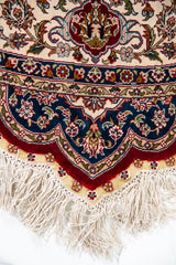 Detalle de guarda y flecos de alfombra persa redonda con diseño floral y tonos azul, beige y rojo