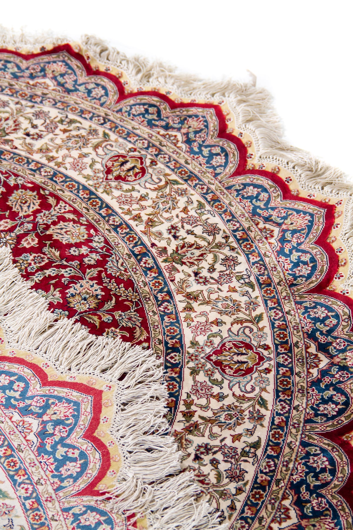 Detalle de textura, guarda y flecos de alfombra persa redonda en tonos rojo, beige y azul