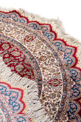 Detalle de textura, guarda y flecos de alfombra persa redonda en tonos rojo, beige y azul