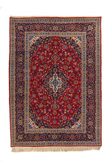 Alfombra oriental rectangular en tonos rojo intenso, azul oscuro y beige con medallón central floral y guarda decorativa clásica