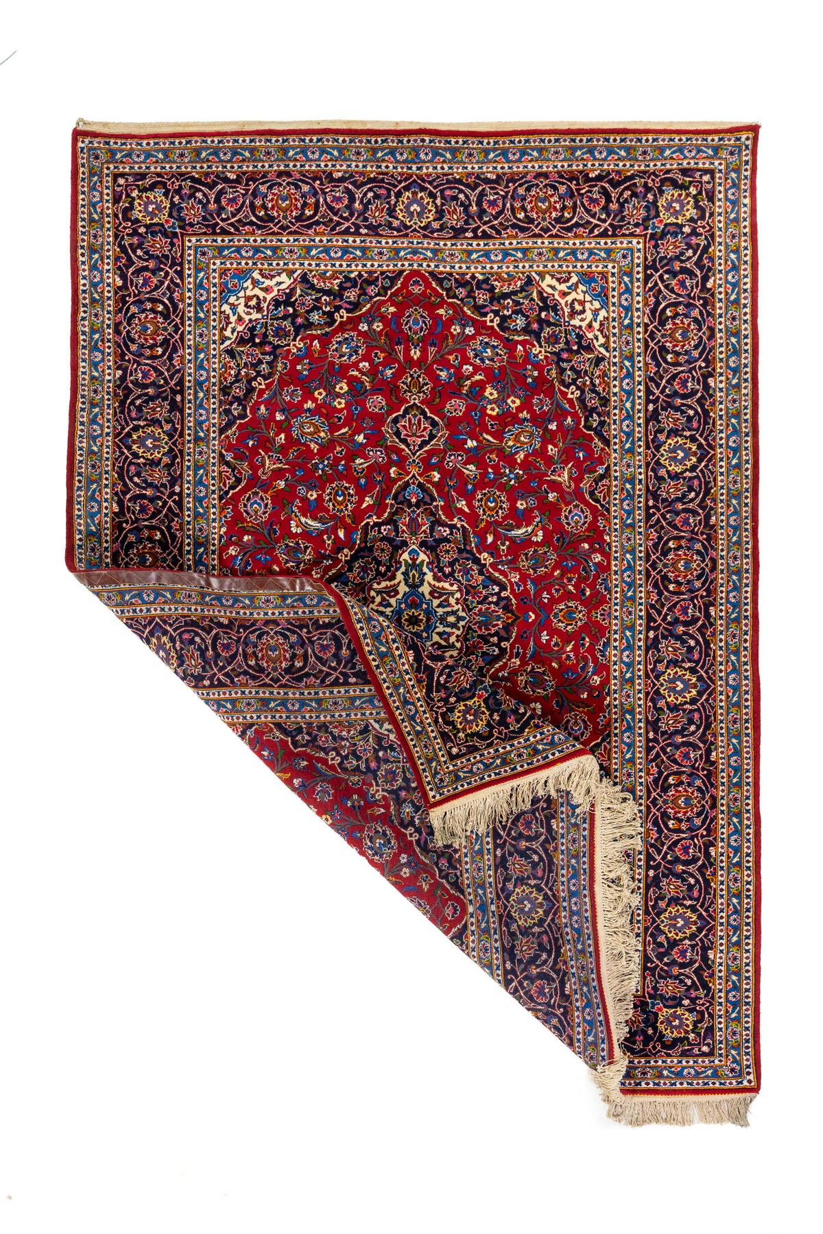 Alfombra clásica rectangular con una esquina doblada que muestra el reverso del tejido, los flecos y el detalle del borde ornamental