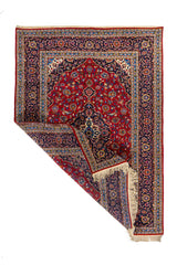 Alfombra clásica rectangular con una esquina doblada que muestra el reverso del tejido, los flecos y el detalle del borde ornamental