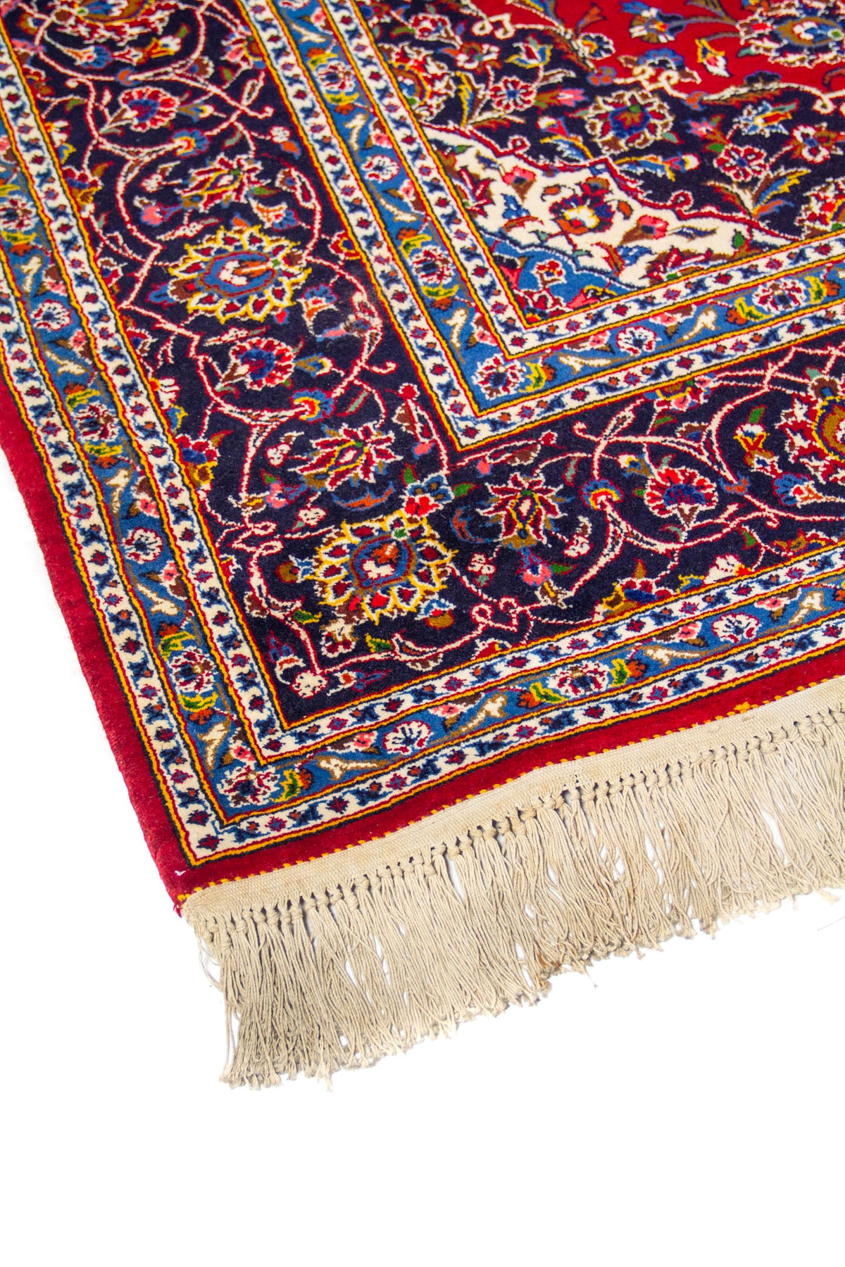 Detalle de esquina de alfombra oriental con fondo rojo, guarda azul floral y flecos claros en uno de los extremos
