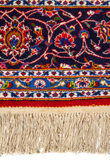 Primer plano de alfombra clásica con motivos florales sobre fondo rojo y borde decorativo en azul, beige y dorado