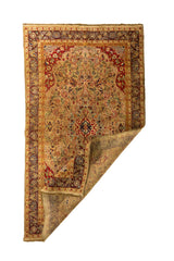 Alfombra persa beige y roja con una esquina doblada que deja ver el reverso del tejido y su elaborado borde floral.