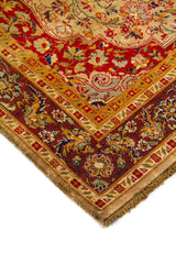 Acercamiento de alfombra oriental con fondo beige, detalles florales en rojo y azul, y borde decorativo con flores y arabescos.