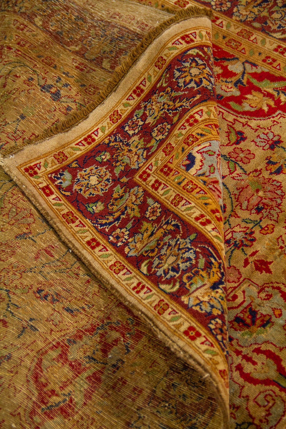 Detalle de alfombra doblada mostrando textura, grosor, reverso del tejido y diseño floral clásico en tonos cálidos.