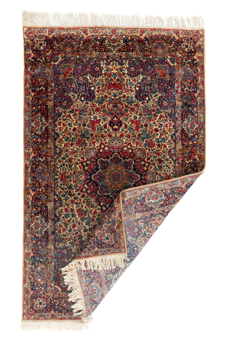 Alfombra persa rectangular doblada con flecos y diseño floral tradicional en tonos beige y azul