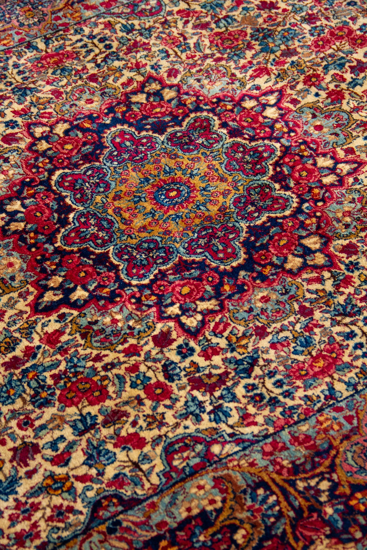 Detalle del medallón central de alfombra persa floral en tonos beige, rojo, azul y dorado