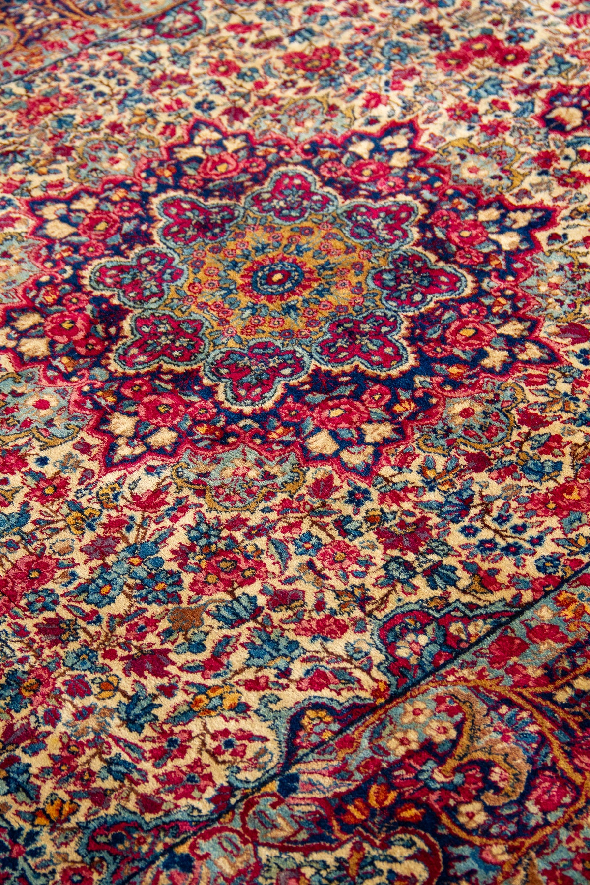 Detalle del medallón central de alfombra persa Kirman con diseño floral en rojo y azul
