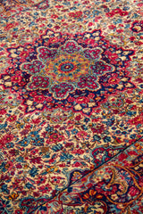 Detalle del medallón central de alfombra persa Kirman con diseño floral en rojo y azul