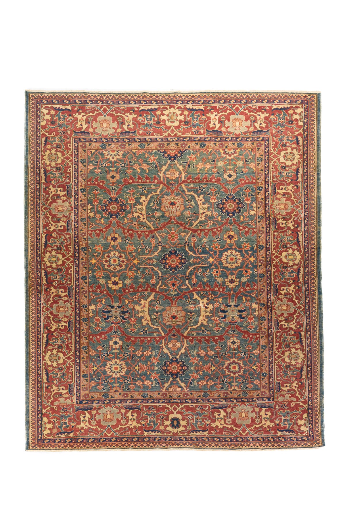 Vista general de una alfombra de inspiración oriental con un campo central en azul, verde y una ancha guarda en tonos rojo. Su composición simétrica combina flores, ramas y ornamentos tradicionales distribuidos con gran equilibrio visual.