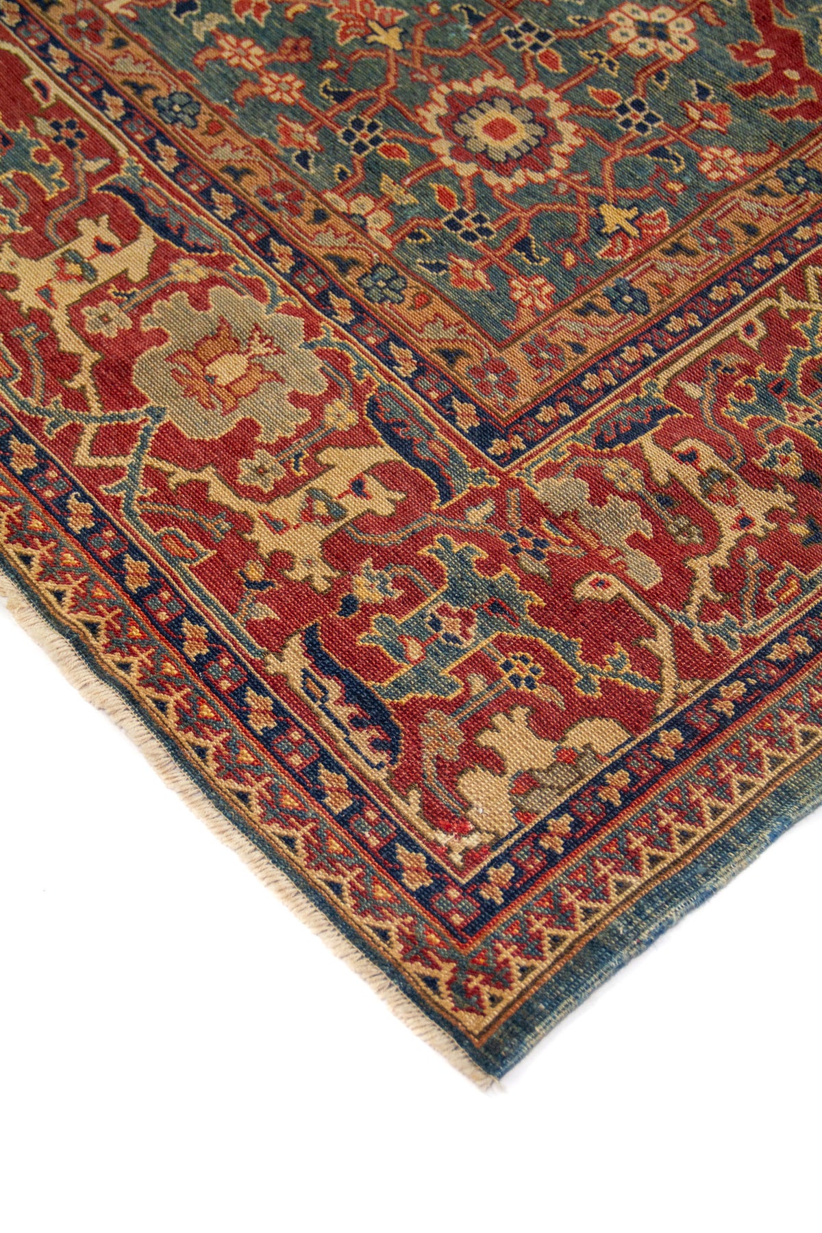 Acercamiento a una esquina donde destacan la riqueza del borde, la definición de las cenefas y la armonía entre el centro azul, verde y la guarda en tonos cálidos. La composición transmite elegancia y tradición.