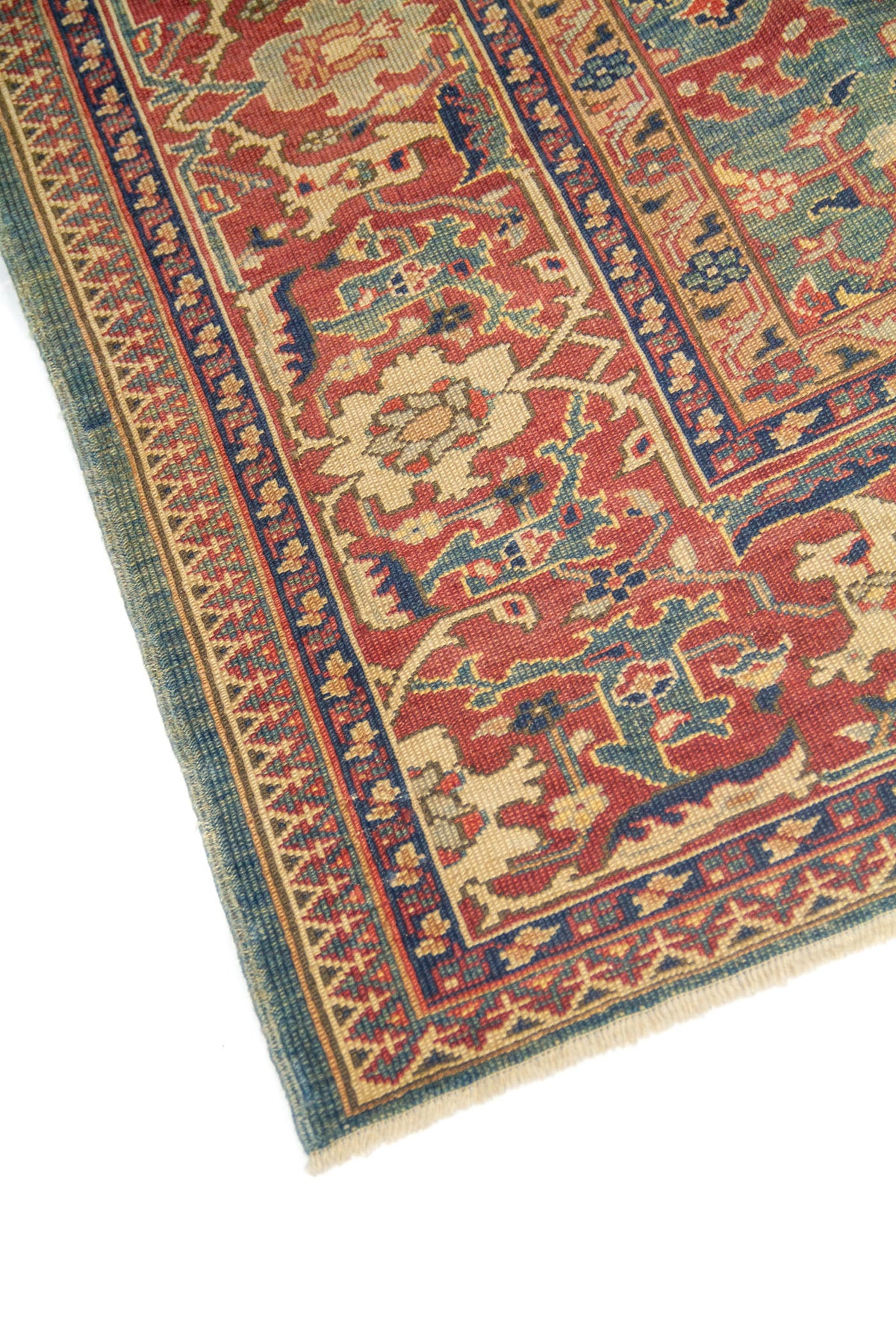 Detalle lateral de alfombra oriental con motivos florales en azul, verde, rojo y beige