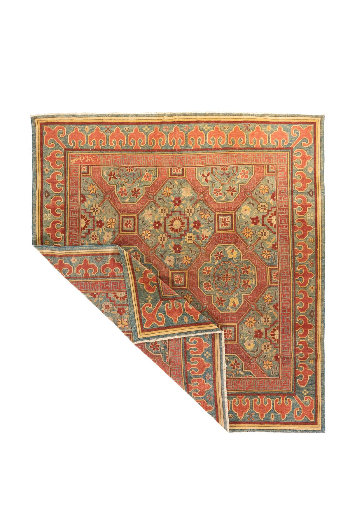 La esquina levantada permite apreciar la caída natural de la alfombra, la flexibilidad del tejido y parte de su reverso. Esta imagen también resalta la continuidad del diseño entre el campo central y los bordes ornamentales.