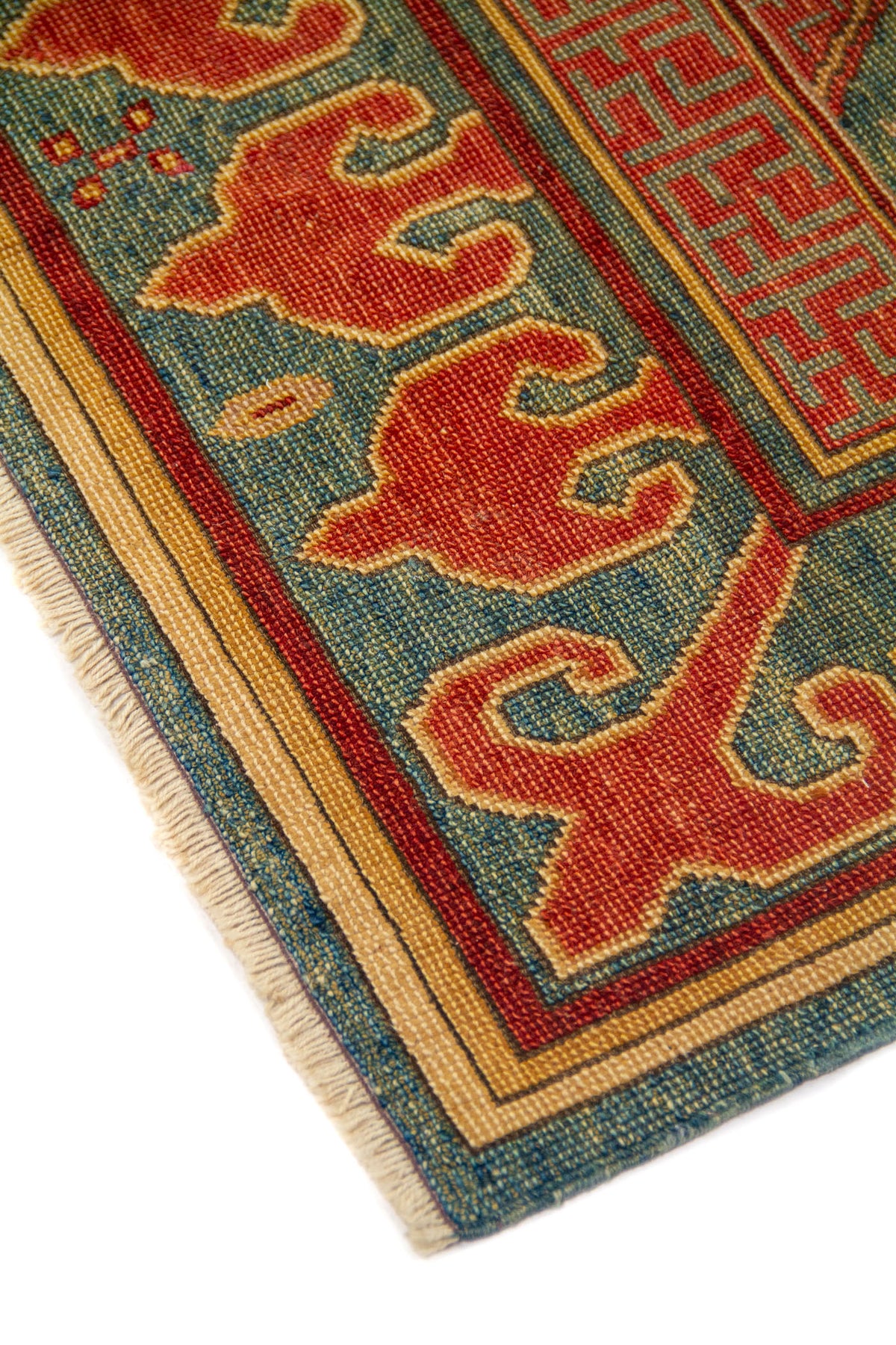 Primer plano de una esquina donde se observan con claridad los bordes, las cenefas y los flecos. La combinación de rojo, beige, azul y verde crea un efecto visual cálido, elegante y muy decorativo.