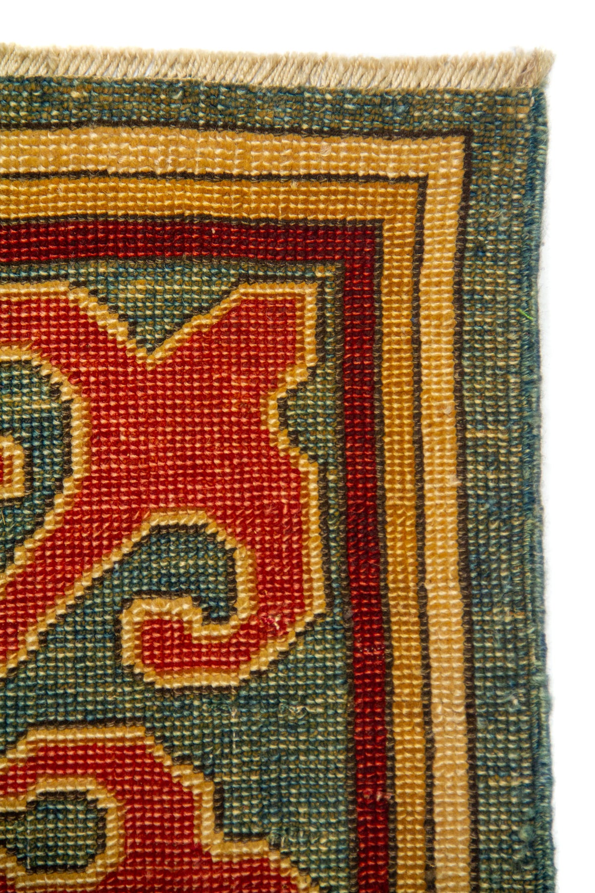 Primer plano de borde de alfombra oriental con guarda geométrica rojo, fondo azul y verde