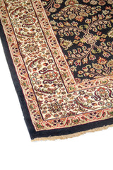 Primer plano de borde de alfombra oriental con guarda blanco suave decorada con arabescos florales sobre fondo negro.