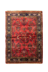 Alfombra clásica de estilo floral con fondo rojo coral, guarda azul marino y motivos ornamentales en tonos beige, verde y dorado.