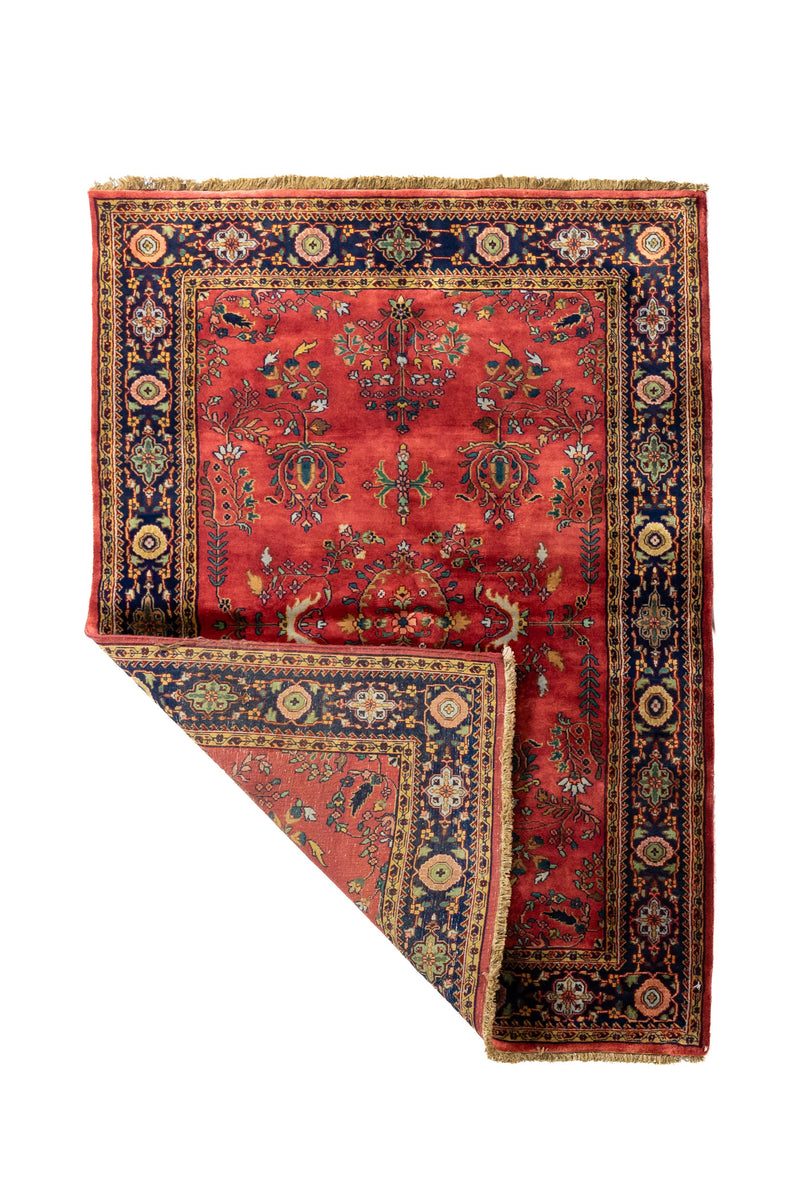 Alfombra floral tradicional con una esquina doblada que permite ver el reverso, el grosor de la pieza y sus flecos artesanales.