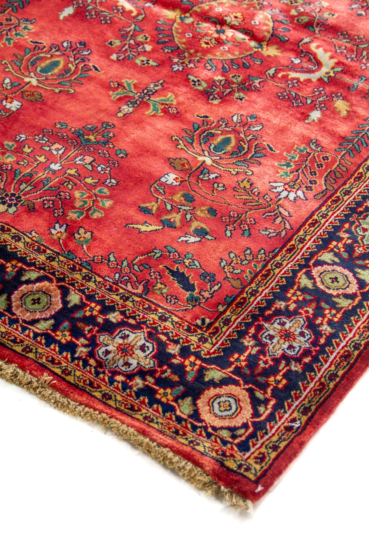 Detalle en esquina de alfombra con fondo rojo intenso, borde azul oscuro y delicados motivos florales de inspiración oriental.