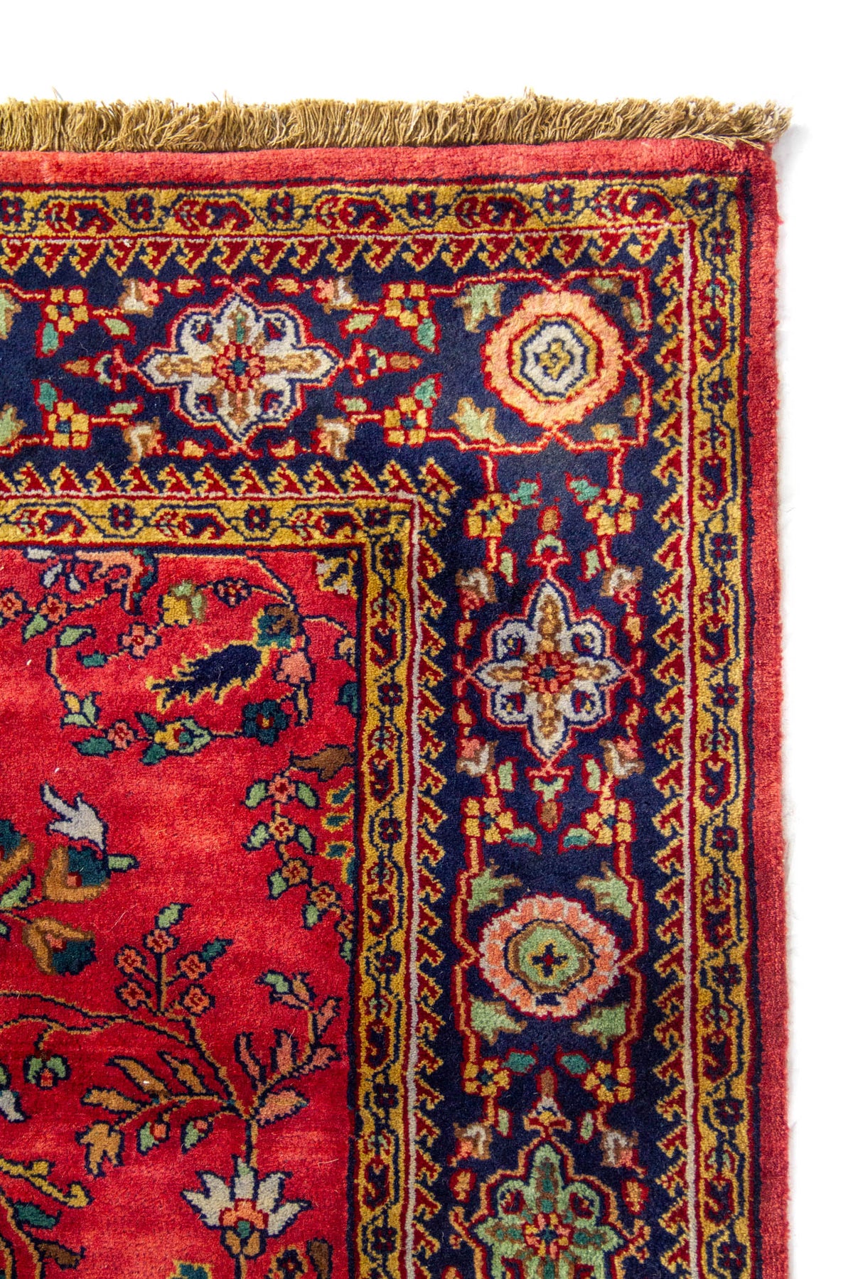 Detalle del borde superior de una alfombra con guarda azul marino, patrones ornamentales multicolor y flecos en tono beige.