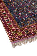 Primer plano de alfombra oriental con fondo azul, pequeños motivos geométricos repetitivos y borde decorativo en rojo, beige y amarillo