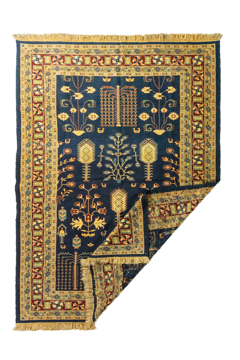 Alfombra oriental azul con una esquina doblada que muestra el reverso del tejido y los flecos laterales