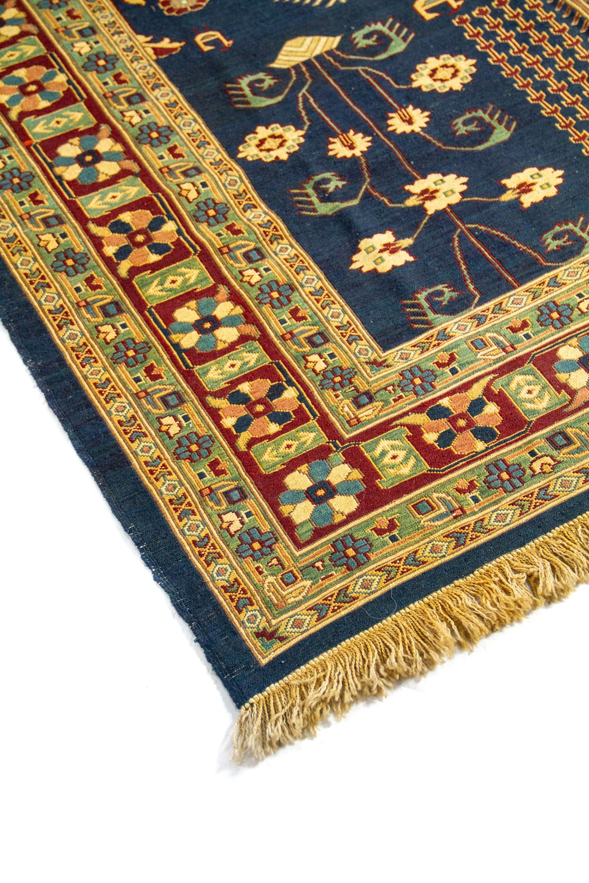 Primer plano de alfombra azul con diseño botánico simétrico y cenefa decorativa en rojo, verde y beige