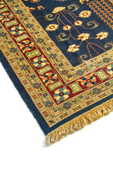 Primer plano de alfombra azul con diseño botánico simétrico y cenefa decorativa en rojo, verde y beige