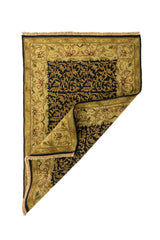 Alfombra rectangular con esquina doblada que muestra el reverso del tejido y el contraste entre el centro oscuro y la guarda en tonos dorados