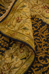 Detalle de alfombra doblada mostrando textura, grosor, acabado de los bordes y diseño ornamental en tonos negro, dorado y beige