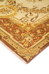 Detalle de esquina de alfombra decorativa con fondo beige, flores delicadas y guarda marrón con motivos vegetales