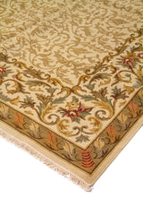 Detalle de esquina de alfombra beige con finos motivos vegetales, flores pequeñas y guarda en tonos verde y rojo