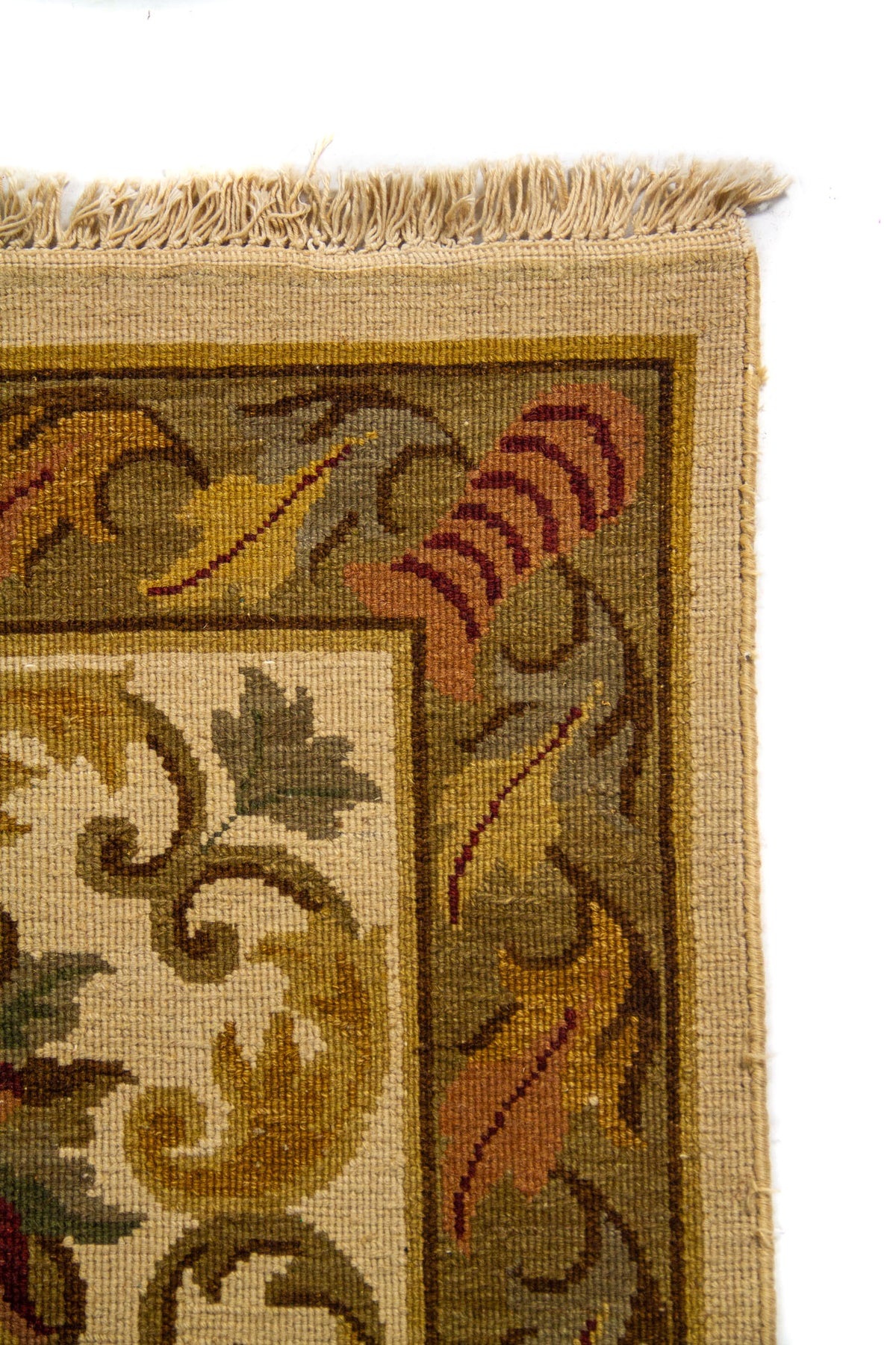 Detalle del borde superior de alfombra clásica con diseño ornamental, hojas estilizadas y acabado con flecos claros