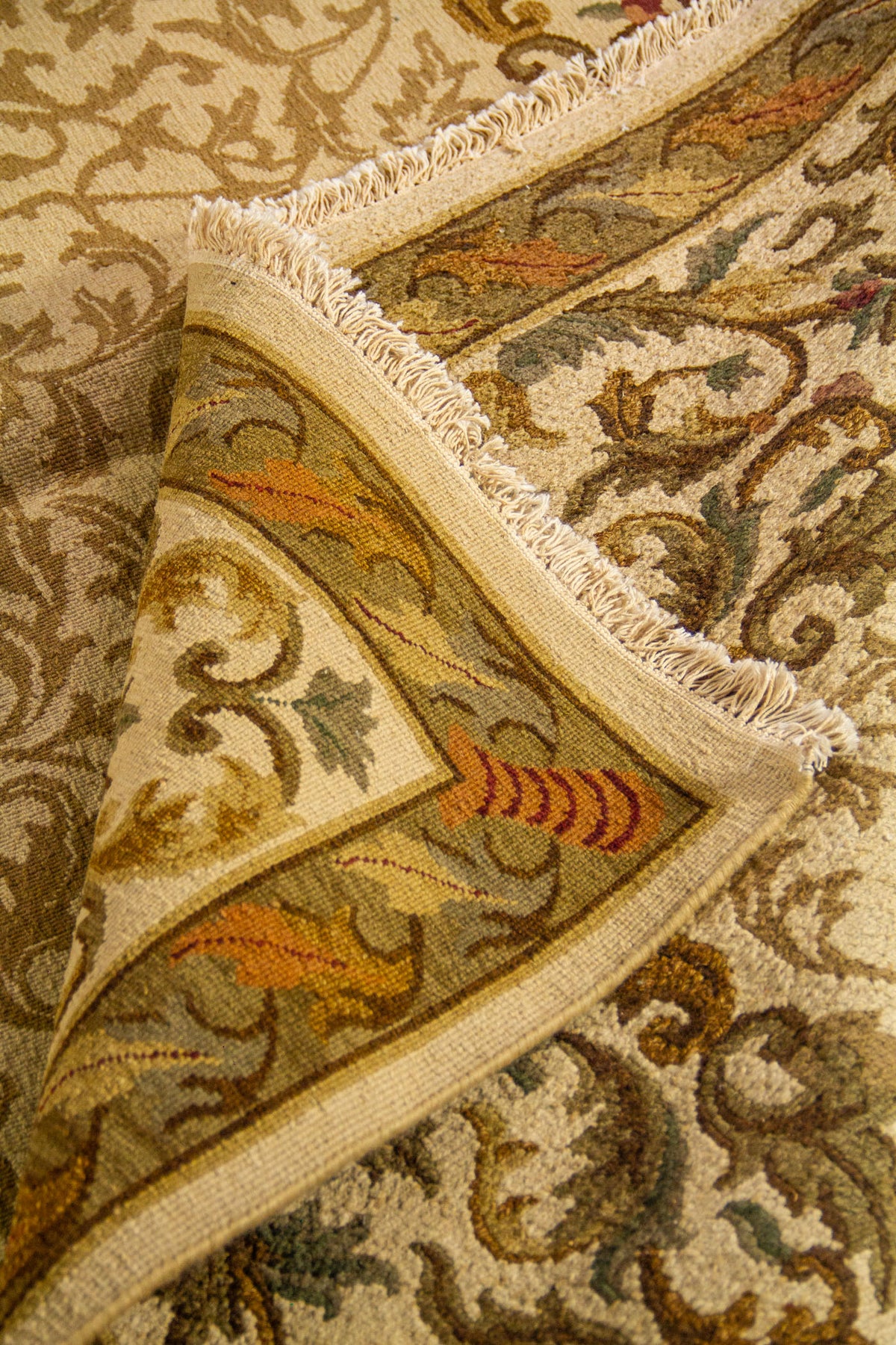 Detalle de alfombra doblada que muestra la textura del tejido, el grosor y los acabados del borde floral decorativo