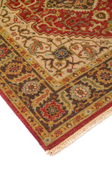 Detalle de esquina de alfombra oriental con medallón rojo, fondo beige y guarda floral geométrica en tonos marrón, azul claro y rojo.