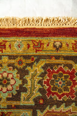 Detalle del borde superior de alfombra oriental con flecos claros y motivos florales geométricos en rojo, marrón, beige y azul.