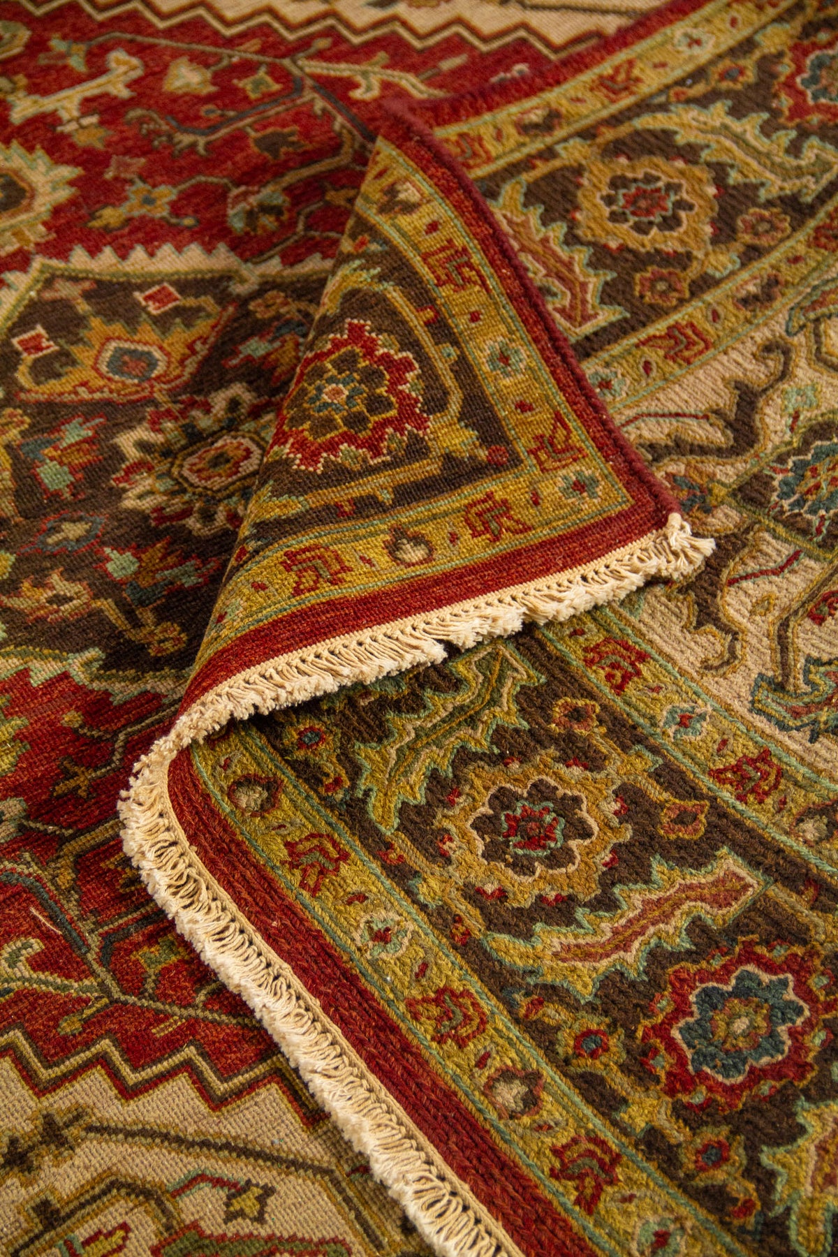Alfombra oriental doblada mostrando la textura del tejido, el reverso y el diseño del borde ornamental con flecos.
