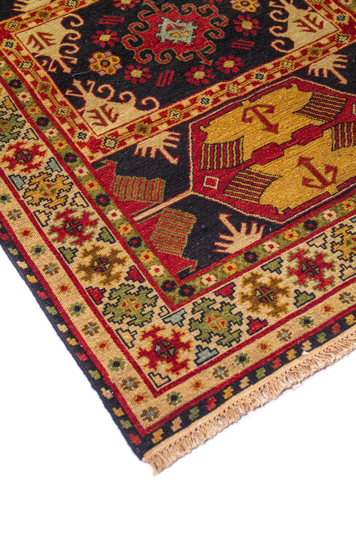 Detalle en ángulo de alfombra con motivos geométricos en rojo, beige, azul oscuro y verde, con flecos visibles en un extremo.