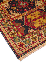 Detalle en ángulo de alfombra con motivos geométricos en rojo, beige, azul oscuro y verde, con flecos visibles en un extremo.