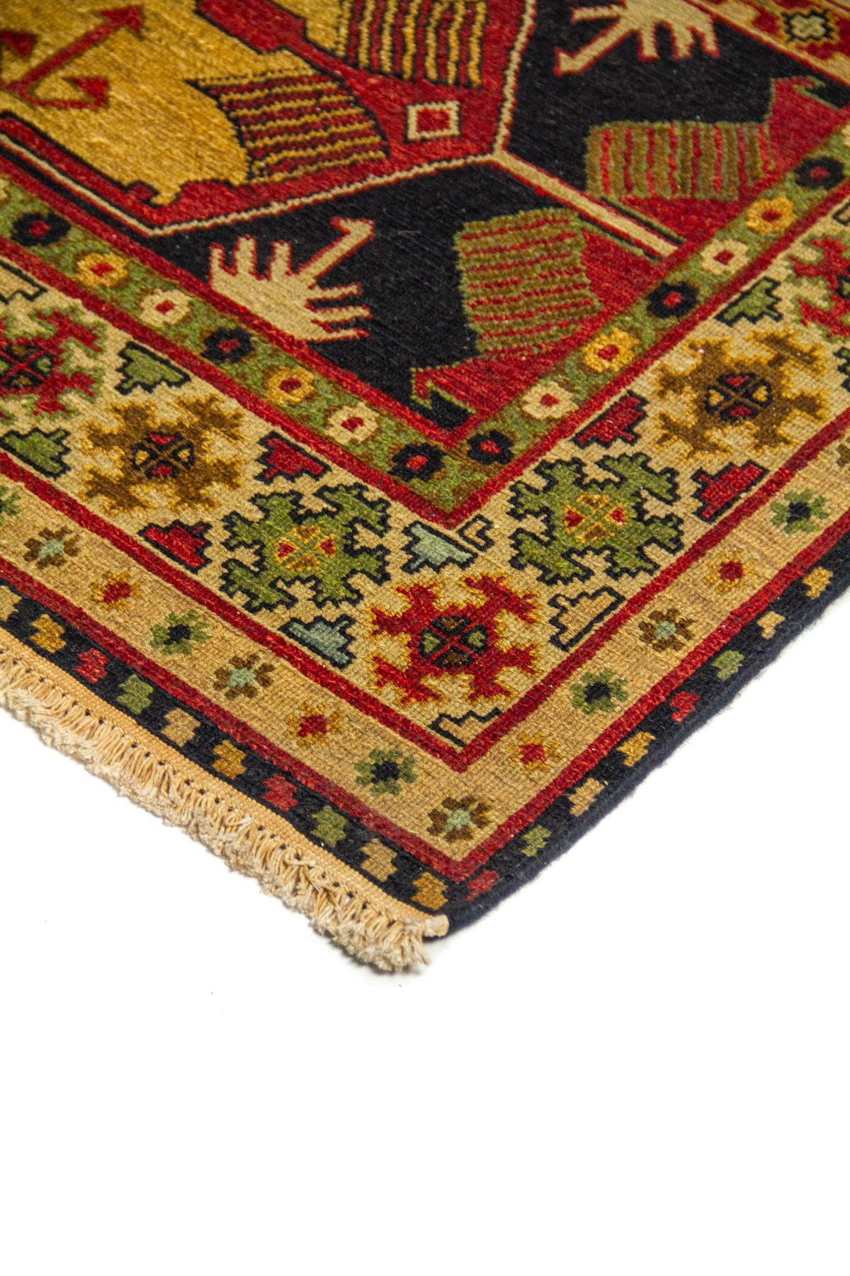 Detalle de esquina de alfombra con borde geométrico en beige, rojo y verde, y diseño central en tonos azul oscuro y dorado.