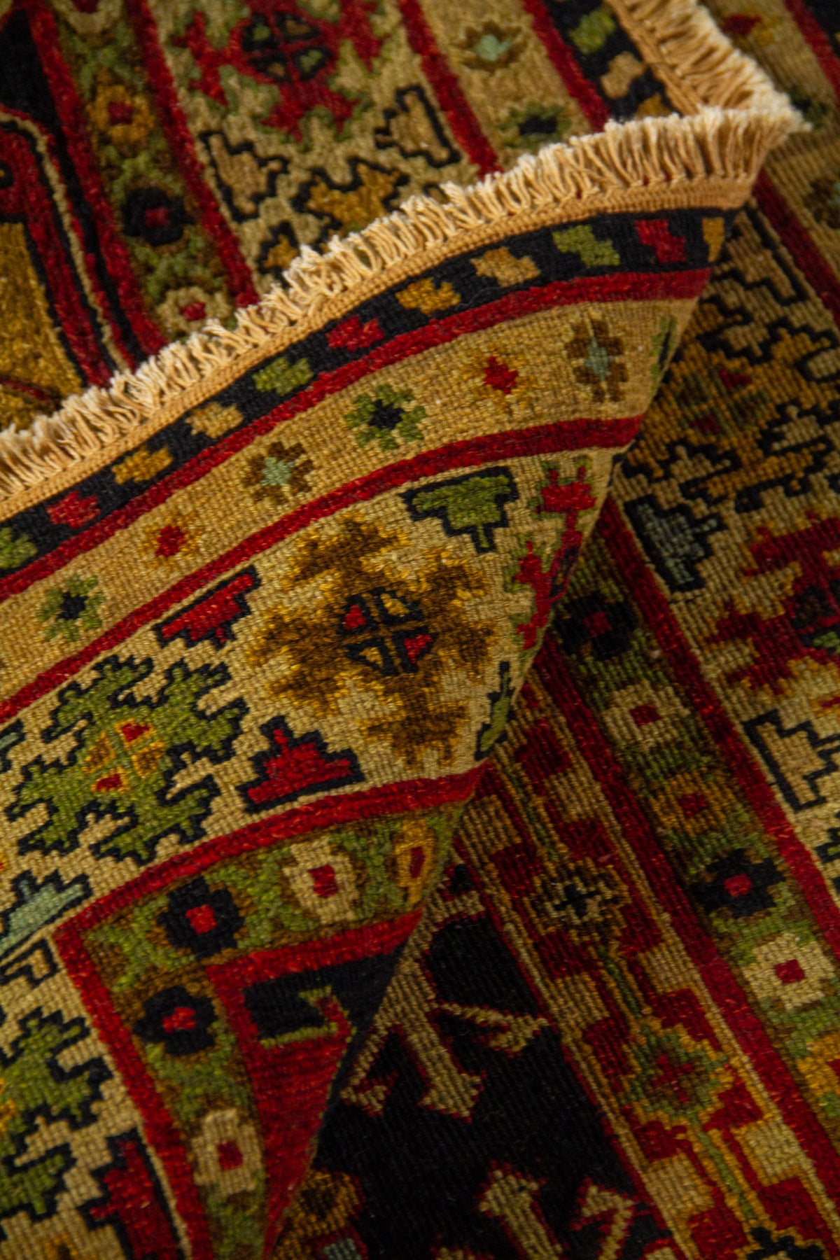 Detalle de alfombra doblada mostrando la textura del tejido, el reverso de la pieza y los flecos en tonos beige.