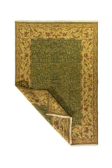 Alfombra tradicional verde oscuro y beige con una esquina doblada que muestra el reverso del tejido y su acabado artesanal