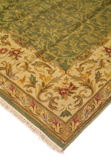 Detalle de esquina de alfombra clásica con fondo verde oscuro, borde beige floral y flecos claros en el extremo